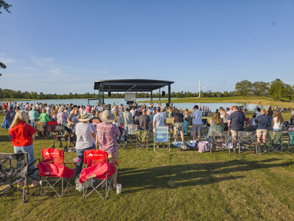 Community gathered in front of amphitheater at Holy Land Farms with Cross in the background.