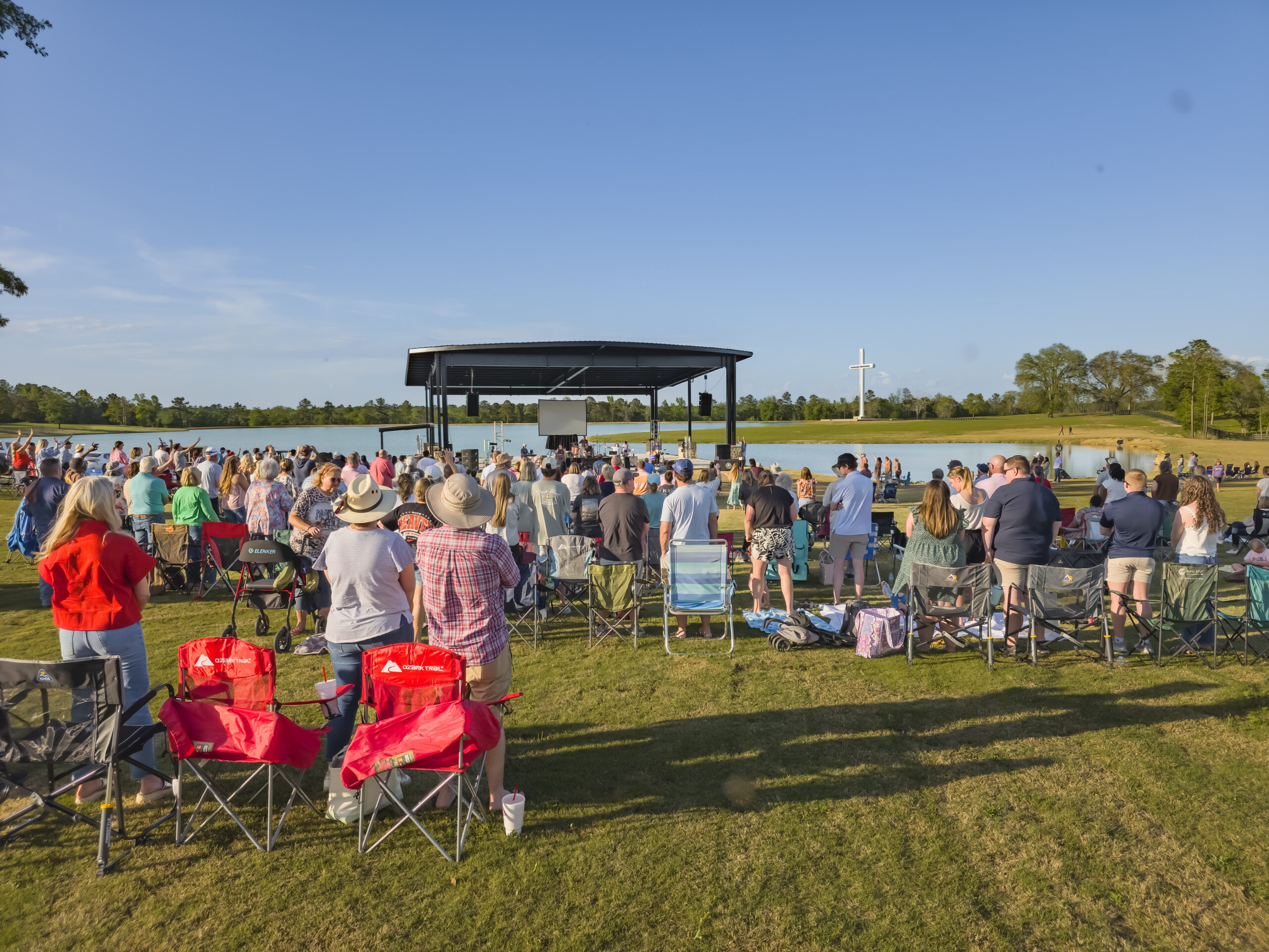 Community gathered in front of amphitheater at Holy Land Farms with Cross in the background.